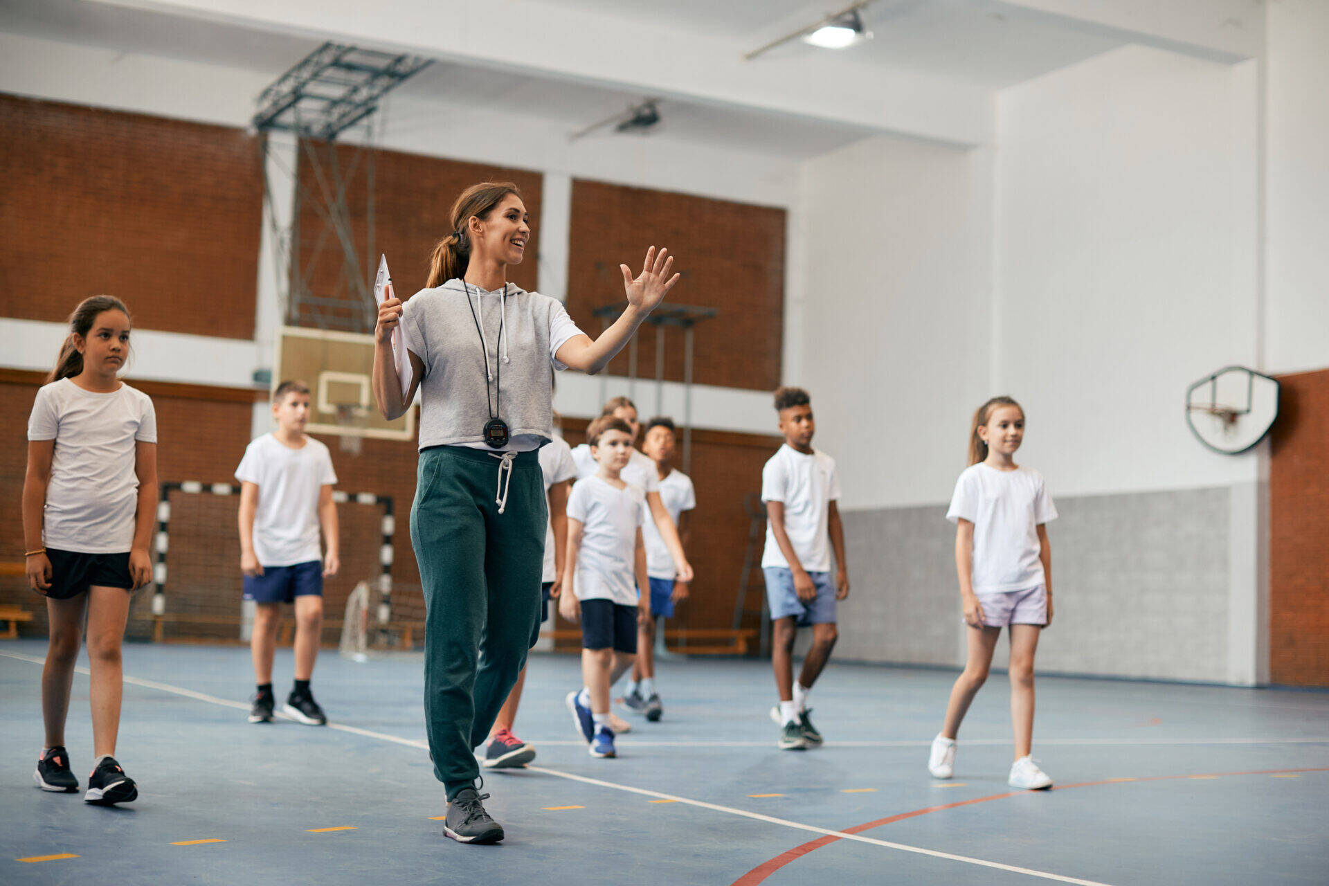 Happy physical education teacher talking to her students during a class at elementary school gym.