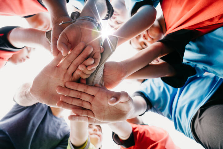 Low angle view of kids Football School Team huddling together. They are putting hands together in circle. Sun beams, lens flare.